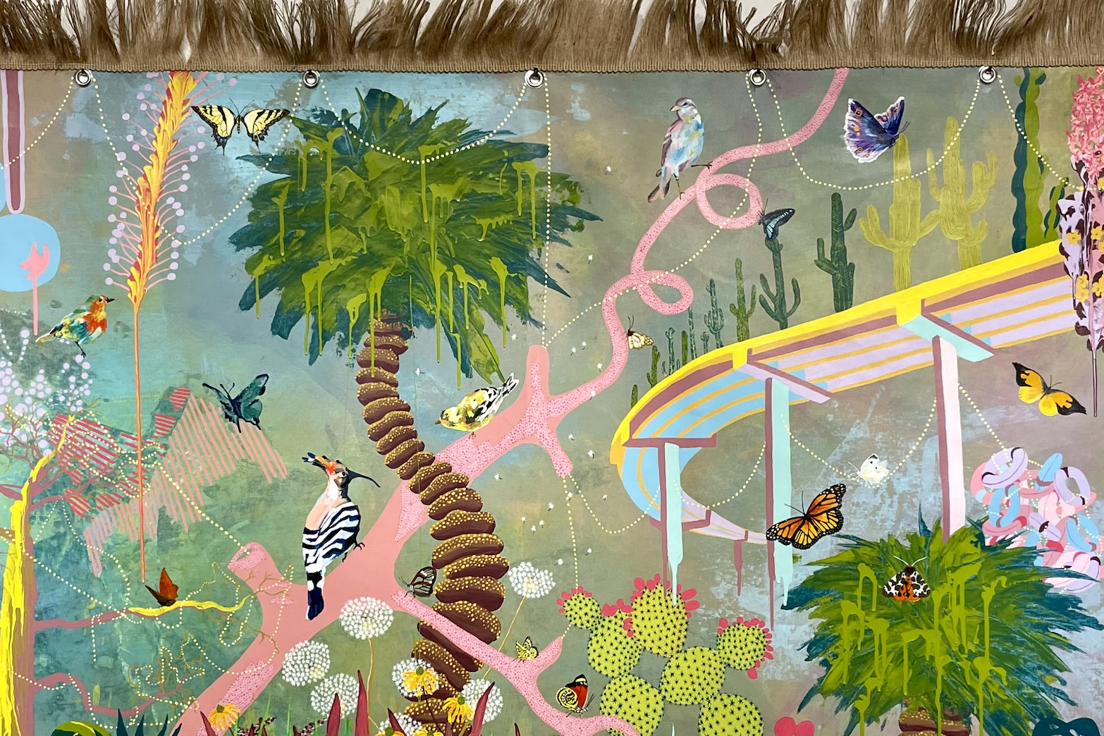 A surreal, vibrant painting of a hazy landscape bordered with brown fringe at the top. It features a stylized palm tree, winding pink branches, green cacti, and a colorful curved structure, with various birds and butterflies scattered throughout the scene
